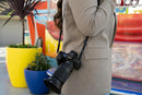 Photographer carrying a Nikon Z mirrorless camera with the NIKKOR Z 28-400mm f/4-8 VR lens and lens hood attached via shoulder strap outdoors