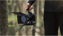 Videographer carrying handheld Canon R6 Mark II rigged with Tilta camera cage top handle and matte box