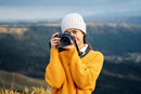 Female photographer holding a Nikon Z camera equipped with the NIKKOR Z 24-105mm f/4-7.1 travel zoom lens against a mountain background